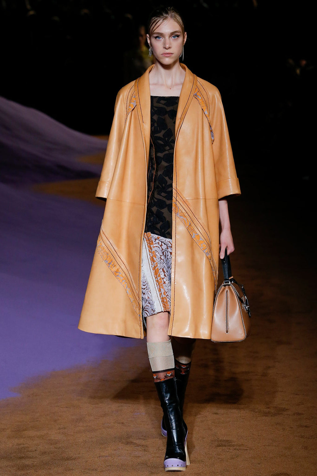Prada leather camel coat hanging on a wooden hanger, showcasing its smooth texture and tailored design.